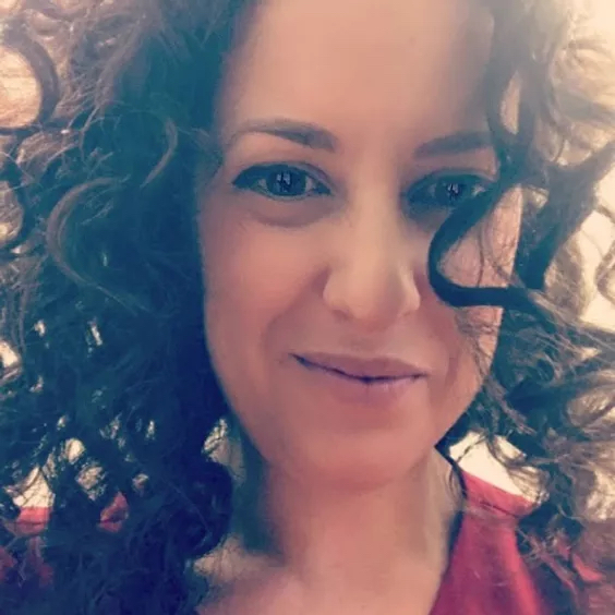 Light-skinned woman with brown curly hair smiling at the camera